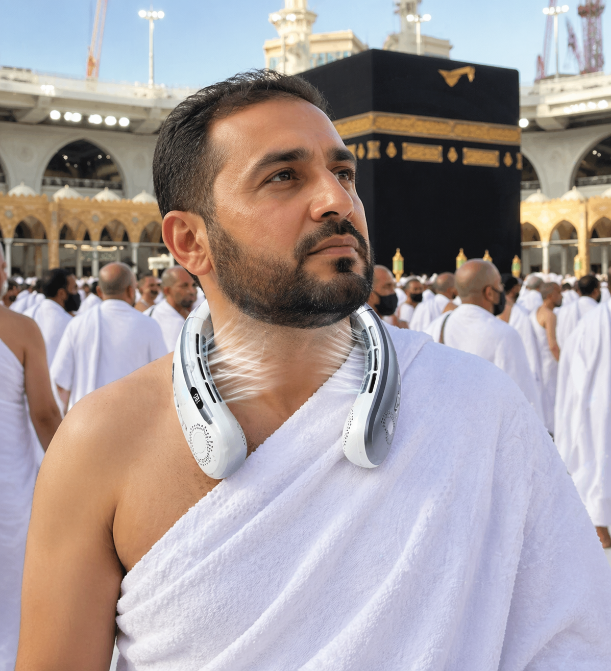 Man in white ihram attire with a White neckband portal cooling device, standing in front of the Kaaba in Mecca.