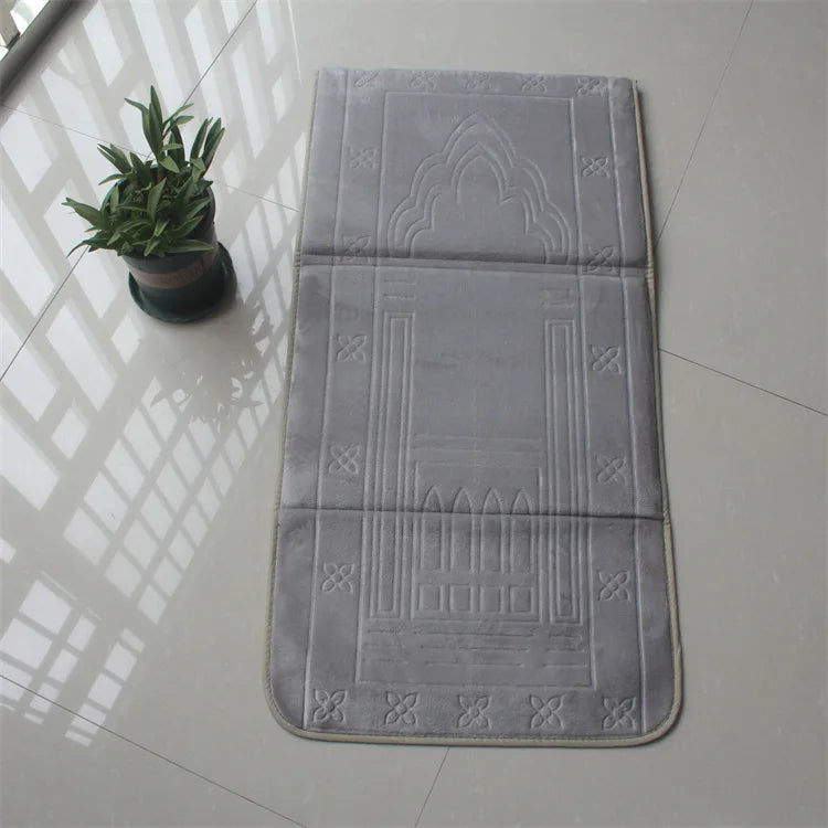 Green soft memory foam Islamic Prayer mat with back rest and  embossed patterns on a tiled floor next to a potted plant.