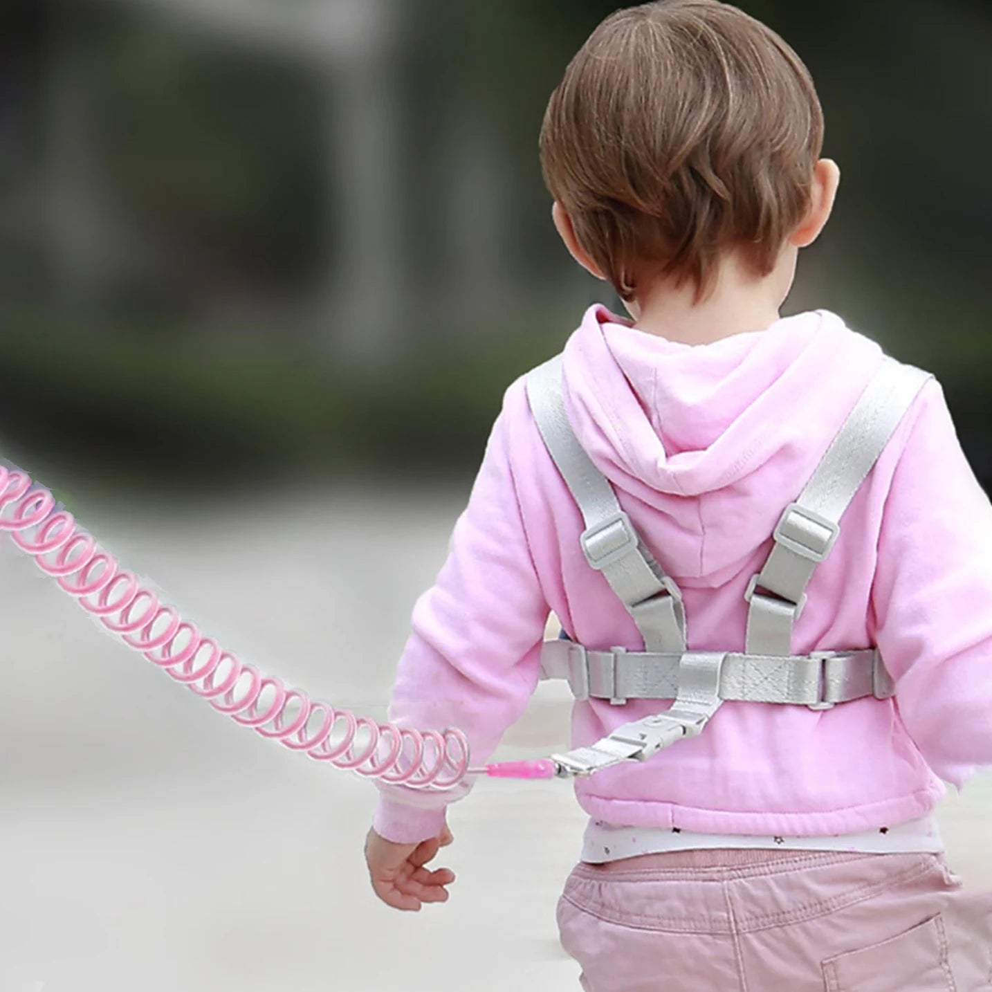Child wearing a pink jacket with a harness and pink leash for hajj and umrah pilgrims, standing outdoors.