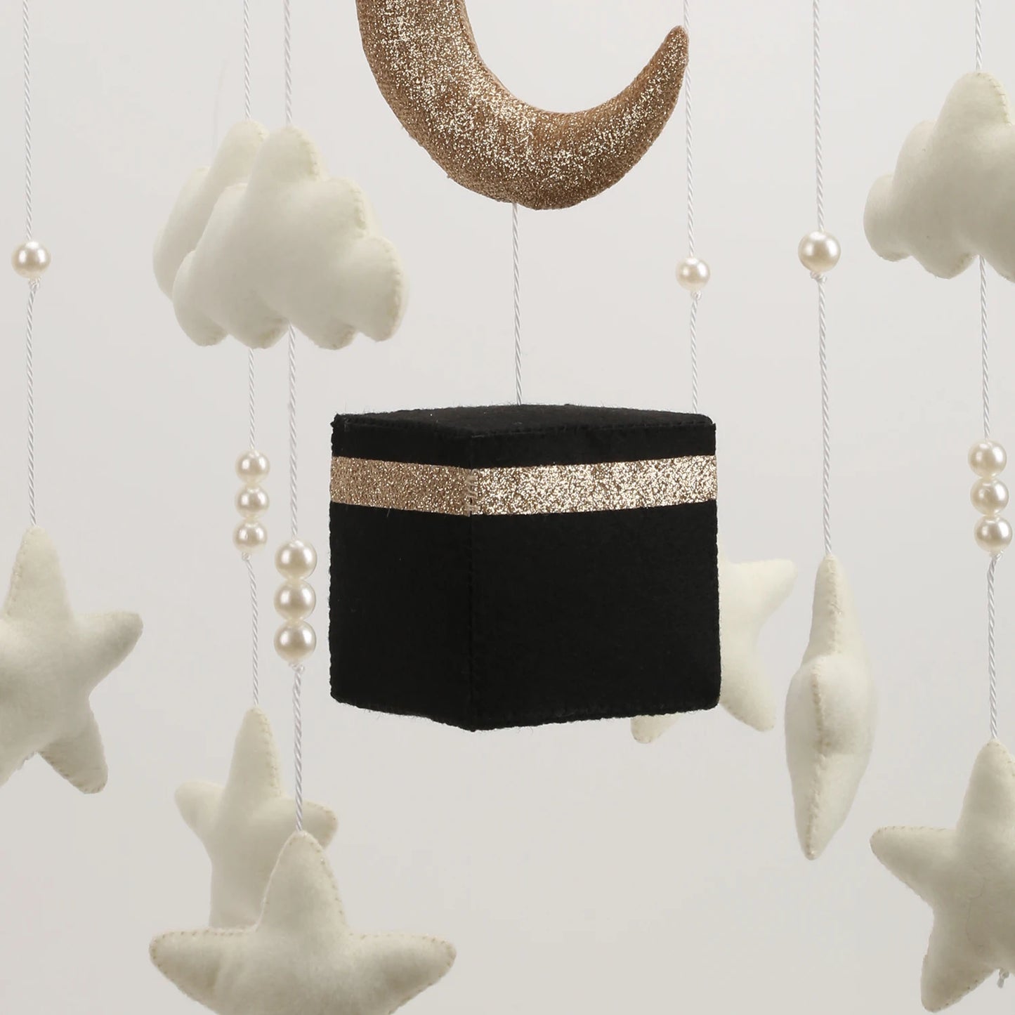 Decorative hanging item resembling a Kaba with gold band, surrounded by stars and clouds on a light background.