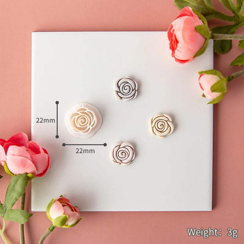 Rose-shaped earrings on a white card with measurements and weight information, surrounded by pink flowers.