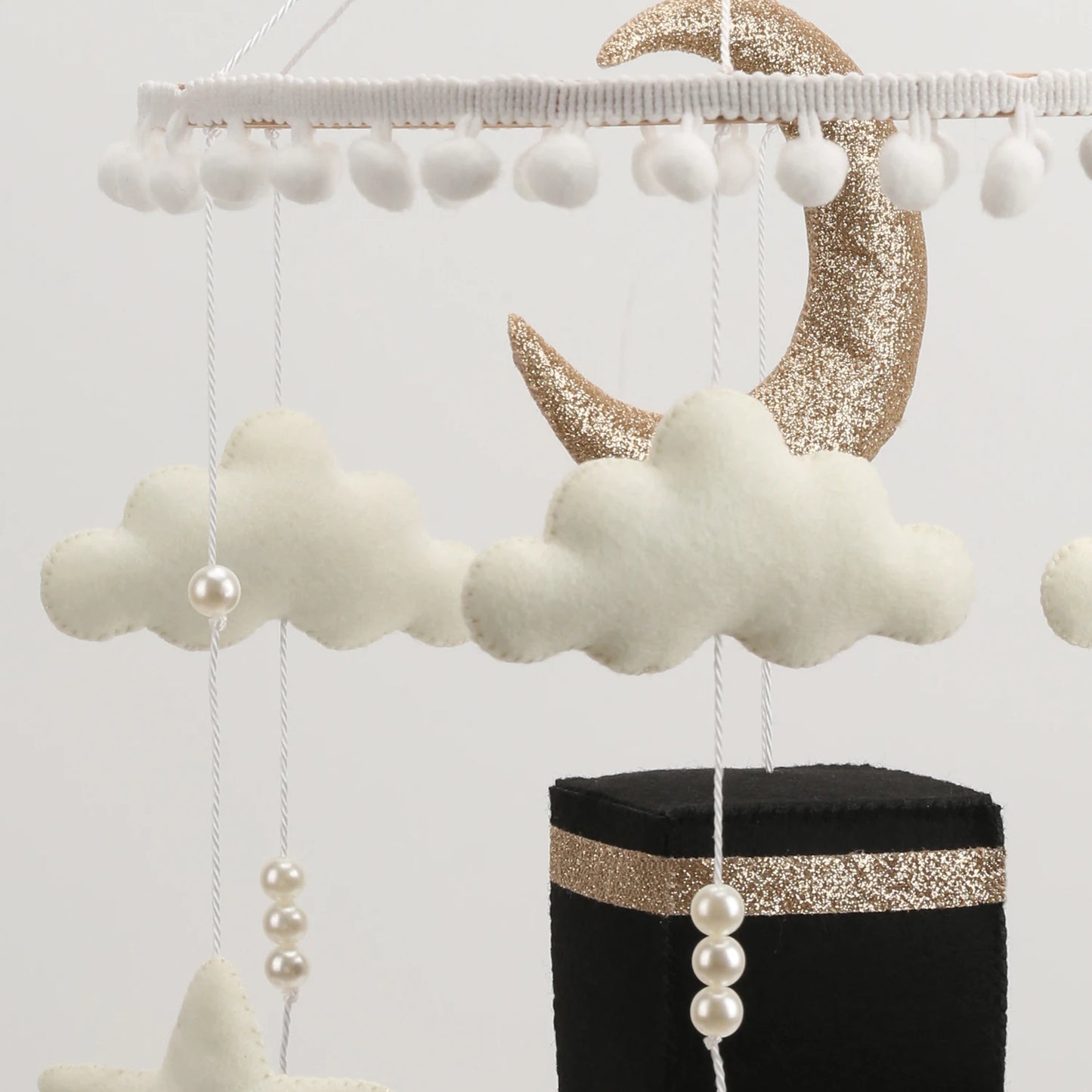 Decorative Islamic crib mobile with clouds, moon, and pearls on a stand against a white background