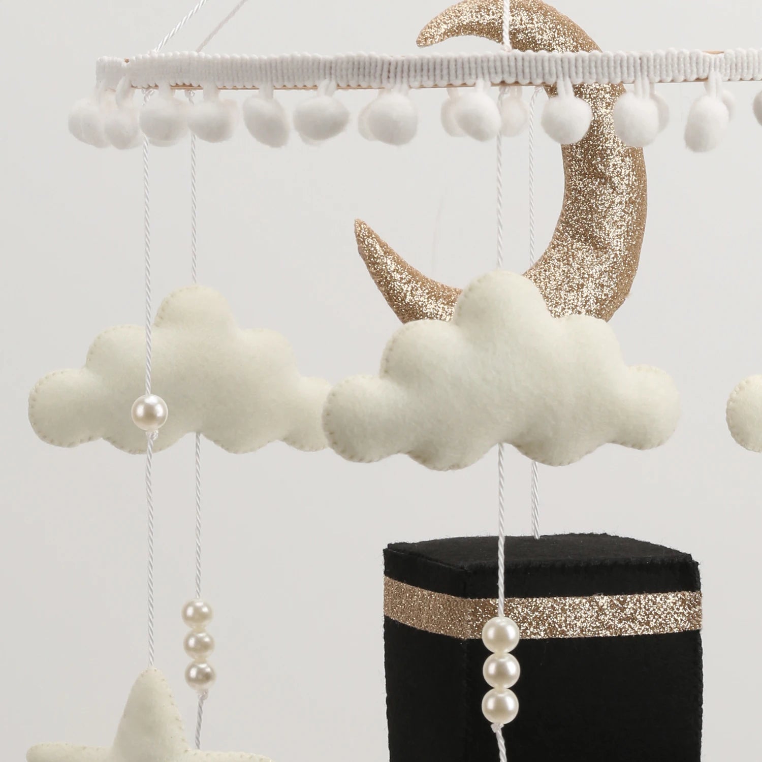 Decorative Islamic crib mobile with clouds, moon, and pearls on a stand against a white background
