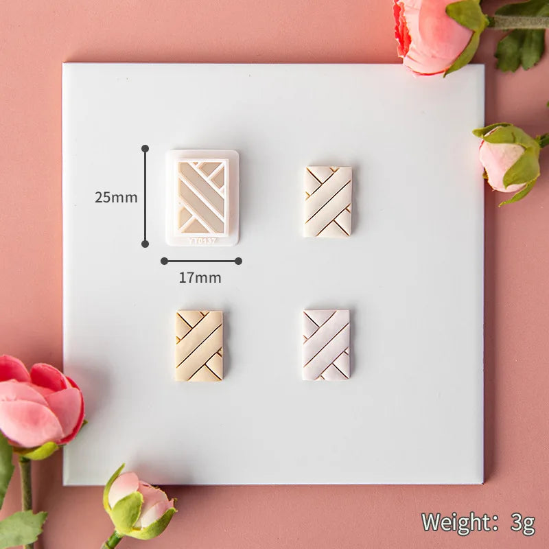 Four geometric-shaped clay bars with measurements and weight on a white card, surrounded by pink flowers.