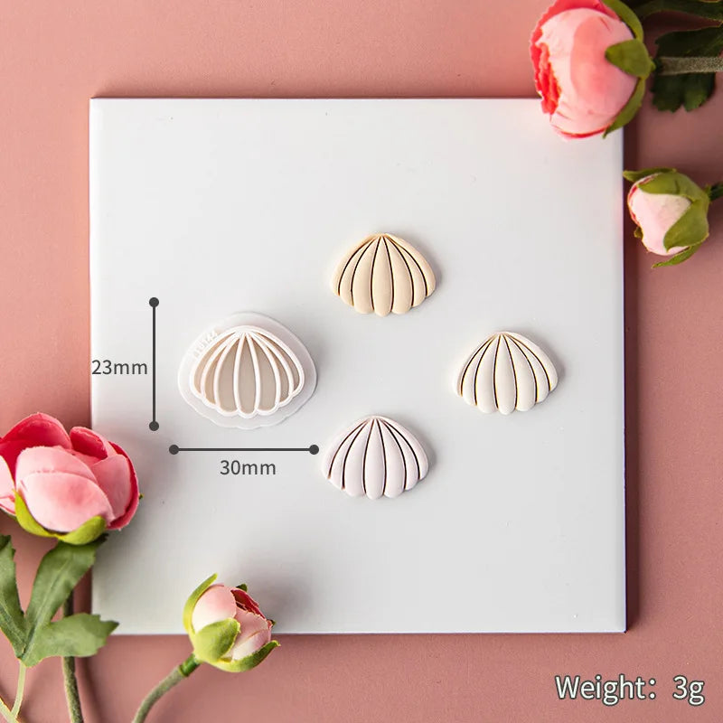 Shell-shaped clay diy mold on a white card with measurements and weight details, surrounded by pink flowers on a pink background.