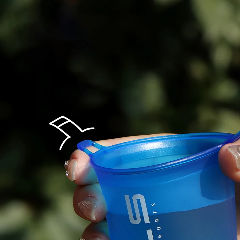 Hand holding a blue collapsible cup with a brand logo against a blurred green background