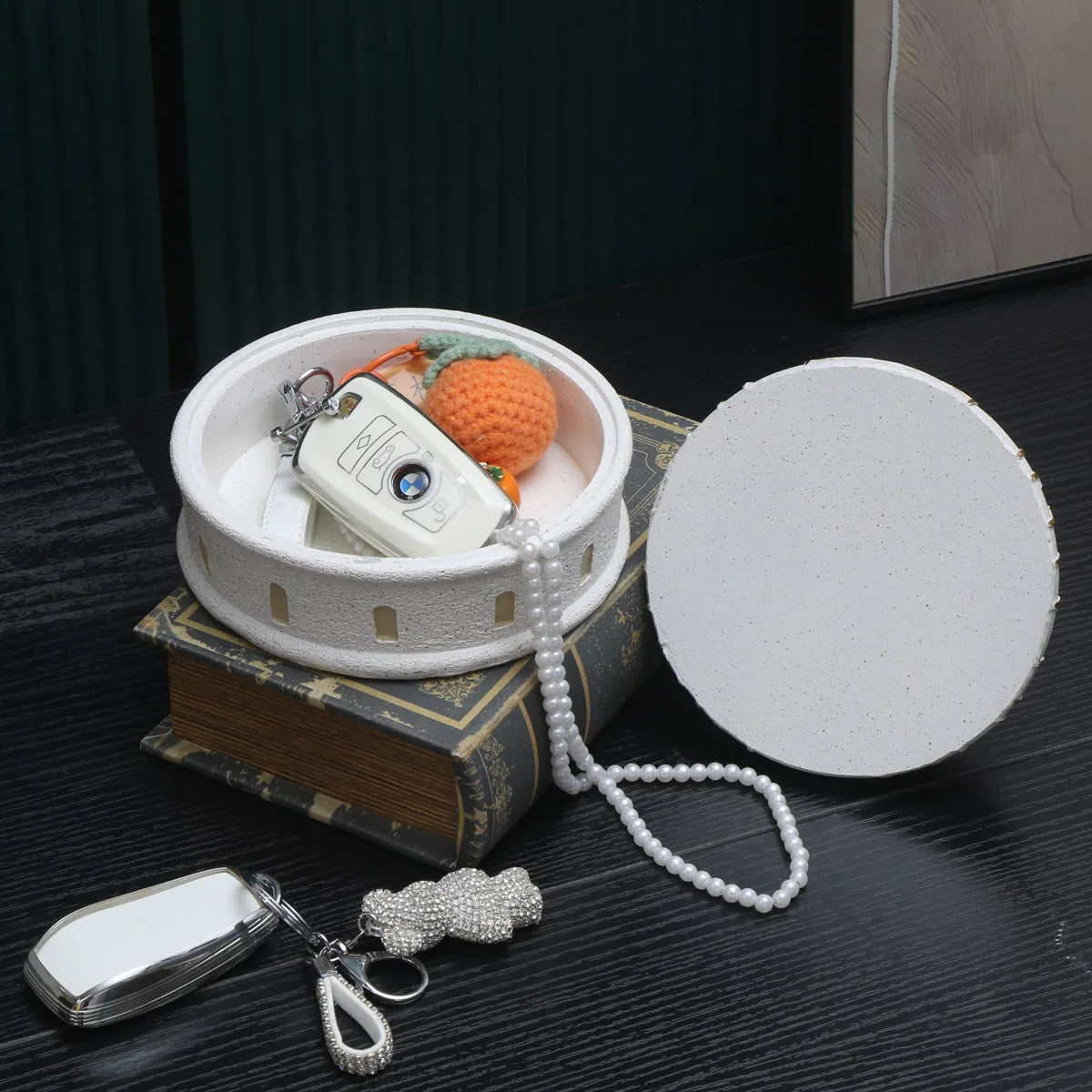 Round white container with a lid, keychain, and small figurine on top of an old book.